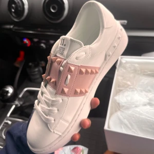 Valentino Rockstud sneakers vit/rosa - Oanvända Rosa Valentino Rockstud sneakers i vitt skinn med ljusrosa band och ikoniska nitar. Ångrade mitt köp, priset går att diskutera! De fyra sista bilderna är lånade från förra säljaren!