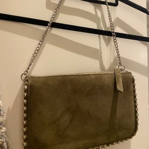 Olivgrön mockaväska Zara - Snygg olivgrön axelväska i mocka med silverfärgad kedjerem och dekorativa nitar längs kanterna. 💕💕💕