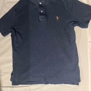 Mörkblå pikétröja från Polo Ralph Lauren - Mörkblå pikétröja från Polo Ralph Lauren i skön pima cotton. Klassisk krage, två knappar och den ikoniska broderade polospelaren på bröstet. Perfekt basic med snygg passform och stilren look. Hör av er vid någon fråga osv. Priset kan gå ner vid snabb affär✅