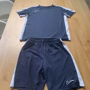 Marinblå Nike Dri-Fit fotbollströja XL - Snygg marinblå fotbollströja från Nike med vita detaljer längs sidorna och ärmarna. Kortärmad modell i Dri-Fit material som andas och håller dig torr under träningen. Ikonisk Nike Swoosh broderad på bröstet. Perfekt för match eller träning.