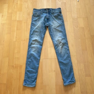 Replay Anbass ljusblå jeans, W29 L32 - Säljer ett par Replay Anbass jeans i ljusblå tvätt med snygga slitningar och klassiska femficksdetaljer. Jeansen har slim passform och raka ben, tillverkade i mjukt denim. Perfekta för dig som gillar en avslappnad men stilren look.