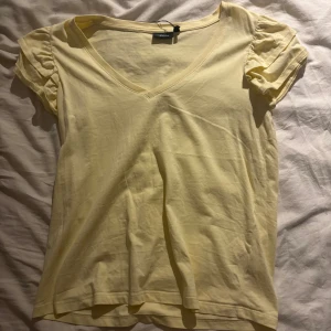 Gul v-ringad topp från KappAhl - Söt ljusgul topp från KappAhl i storlek S. Modellen har v-ringning, korta puffärmar och är gjord i mjuk bomull. Perfekt när du vill ha något enkelt men ändå gulligt.