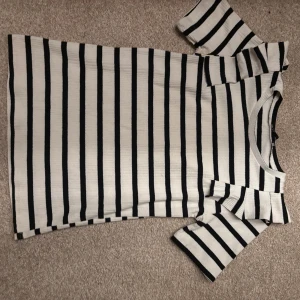 Randig t-shirt i svart och vitt - Snygg t-shirt med svarta och vita ränder. Modellen har korta ärmar och rund halsringning. Perfekt för en chill och stilren look. Materialet känns mjukt och skönt mot huden.