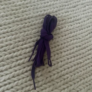 Lila skosnören i textil - Säljer ett par lila skosnören i textil, perfekta för att ge dina sneakers eller kängor en personlig touch. De är platta och har klassiska plasttips i ändarna. Passar till de flesta skotyper och är enkla att trä i.