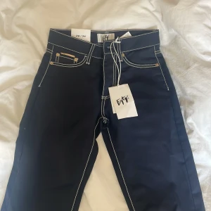 Svarta byxor från Eytys med kontrastsömmar - Snygga svarta byxor från Eytys med vita kontrastsömmar och klassisk femficksdesign. Byxorna har raka ben och en cool etikett på bakfickan med grafiskt tryck. Helt oanvända