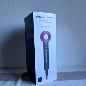 Dyson Supersonic hårfön - Dyson Supersonic hårfön i snygg grå och metallic rosa design. Ergonomiskt handtag, rundad form och modern look. Levereras i originalkartong med sladd. Perfekt för dig som vill ha snabb och skonsam hårtorkning med stil.