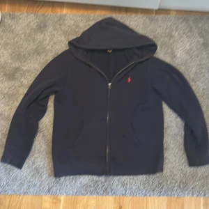 Mörkblå zip hoodie från Ralph lauren - En stilren mörkblå ziphoodie från polo Ralph lauren i storlek 14-16 vilket motsvarar xs, tröjan är perfekt för en stilren vardagslook, säljs i mycket bra skick inga skador. Ps priset är hugget i sten 