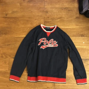 Ralph lauren tröja  - Tvär fet mörkblå långärmad tröja från Polo Ralph Lauren med röd och vit logga framtill. Tröjan har röda och vita detaljer vid hals, ärmslut och nederkant.