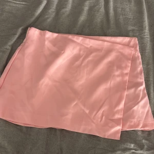 Ljusrosa omlottkjol från SHEIN - Superfin ljusrosa kortkjol från SHEIN i omlottmodell. Kjolen har en slät, glansig yta och är tillverkad i ett tunt, mjukt material som ger en snygg flowy känsla. Perfekt att styla med en crop top eller oversized hoodie.