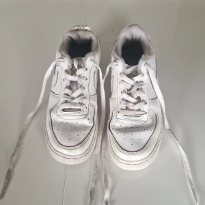 Nike Air Force 1 vita sneakers strl 36.5 - Klassiska Nike Air Force 1 i helvitt skinn med perforerad tå, rund tå och platt sula. Snygg low cut-modell med tydlig swoosh-logga på sidan och vita snören. Perfekta för dig som gillar en clean och tidlös streetstil. Kommer med sko låda.