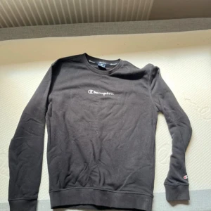 Svart Champion sweatshirt i bomull - Svart sweatshirt från Champion med klassisk logga på bröstet och ärmen. Tröjan har rund halsringning, ribbade muddar och är tillverkad i mjuk bomull. Perfekt för en chill och sportig stil.