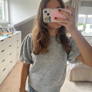 Grå stickad tröja från Gina Tricot - Superfin ljusgrå stickad tröja från Gina Tricot med puffiga korta ärmar och rund halsringning. Tröjan har en mjuk känsla och ribbade kanter vid hals och nederkant. Perfekt för lager-på-lager och chill vibes.