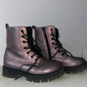 Glittriga boots från Dinsko, stl 31 - Säljer ett par glittriga boots från Dinsko i metallic-lila med svarta snören och grov sula. Skorna har dragkedja på sidan för enkel påtagning och cool look. Perfekta för dig som vill sticka ut med din stil. Ett par boots för barn med olika färger på. Meddela gärna om ni vill ha mer info! 💕