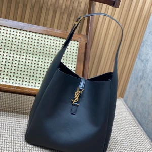 Svart axelväska från Saint Laurent - Snygg svart axelväska från Saint Laurent i äkta skinn med guldiga detaljer och ikoniskt YSL-spänne framtill. Väskan har justerbart axelband med guldfärgat spänne och en stilren, rymlig design som passar perfekt till din vardagsstil.