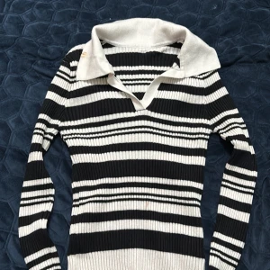 Randig ribbad tröja från Dazy - Säljer en svartvit randig ribbad tröja från Dazy i storlek S. Tröjan har lång ärm, bred krage och v-ringning. Den är figurnära och har en snygg, klassisk look med tydliga ränder och stretchigt material.