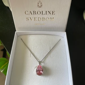 Halsband Caroline Svedbom  - Jättefint halsband från Caroline Svedbom med en i silverfärgad kedja och kritstall berlock i färgen light rose. Kommer i originalask! Fick halsbandet i vintras men har inte använt de så mycket, har aldrig duschat eller badat med det!