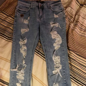 Philipp Plein ljusblå ripped jeans - Ljusblå jeans från Philipp Plein med kraftigt slitna och trasiga detaljer framtill. Klassisk femficksmodell med patch och metallmärke på bakfickan. Skinny fit och låg midja, perfekt för en edgy streetstil.                                      Påprovade av och på!