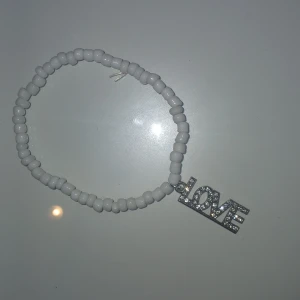 Vitt pärlarmband med LOVE-berlock - Superfint armband med vita pärlor och en glittrig silverfärgad berlock där det står LOVE. Perfekt accessoar för att ge din outfit lite extra bling och kärleksvibe. Stretchig modell som passar de flesta handleder.