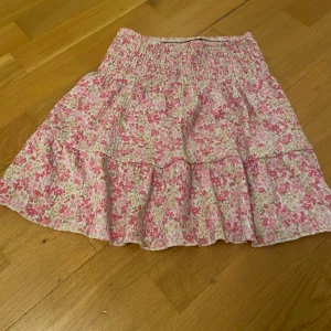 Blommig volangkjol från Gina Tricot - Supersöt kort kjol från Gina Tricot i blommigt mönster med rosa och vita toner. Kjolen har volanger och resår i midjan för en bekväm passform. Perfekt för dig som gillar en feminin och somrig stil.