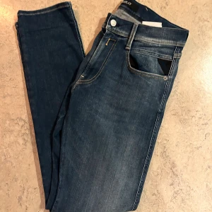 Blåa Replay Anbass jeans  - Säljer ett par helt nya mörkblå Replay Anbass jeans i storlek 32/32. Jeansen har en slim passform med klassisk femficksdesign och snygga detaljer vid fickorna. Tillverkade i stretchigt jeansmaterial för extra komfort. Perfekta för dig som gillar en modern och stilren look.