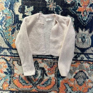 Beige stickad kofta med lång ärm - Säljer en söt, kort och stickad beige kofta med lång ärm. Koftan har en öppen front och är gjord i ett grovstickat material som ger en mysig känsla. Perfekt att slänga över en topp för en chill look.