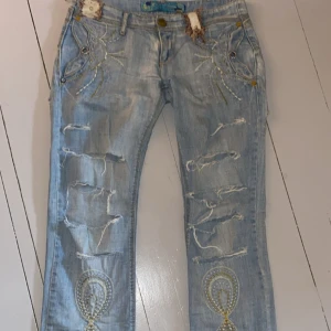 Ljusblå slitna jeans - Unika ljusblå jeans med slitningar och hål framtill. Jeansen har broderingar samt dekorativa sömmar i olika färger. Raka ben och väldigt låg midja. Perfekta för dig som vill sticka ut samt ha en sann 2000s känsla! Skriv för mått eller fler bilder🩵