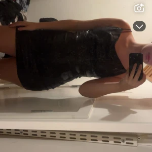 Svart glittrig kort klänning - Säljer en svart glittrig kort klänning med smala axelband och figurnära passform. Perfekt för dig som vill sticka ut med en snygg och trendig look. Klänningen har en enkel men elegant design med glittrande material som fångar ljuset.