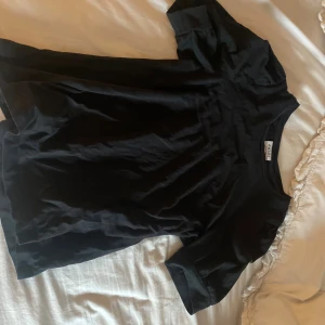 Svart t-shirt från Aware by Vero Moda - En svart basic t-shirt från Aware by Vero Moda i mjuk bomull. Klassisk rund halsringning och korta ärmar med lätt uppvikt kant. Perfekt till jeans eller kjol för en clean look.