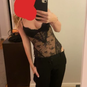 Svart spetskorsett med tunna axelband - Säljer en svart body från HM med tunna justerbara axelband och vacker spets över hela plagget. Den har vadderade kupor, genomskinliga meshpartier och knäppning i grenen. Perfekt för dig som vill ha en edgy och snygg look. stolek 75A, och använd en gång endast❤️