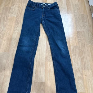 Mörkblå raka jeans i storlek 140 - Snygga mörkblå jeans med klassisk rak passform och fem fickor. Jeansen har gul kontrastsöm och är tillverkade i ett slitstarkt denimtyg. Perfekta för dig som gillar en enkel och tidlös stil.