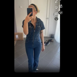 Blå jeans jumpsuit med dragkedja - Snygg blå jeans jumpsuit med korta ärmar, krage och hel dragkedja framtill. Den är i ett jättebra skick då den aldrig är använd. 