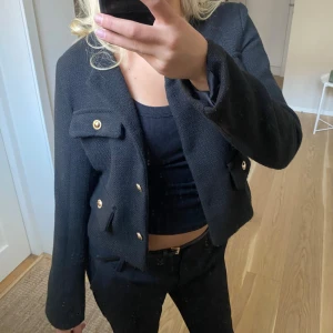 Svart kavajjacka - Säljer en svart kavajjacka med snygga guldknappar och fyra fickor framtill. Jackan är croppad och har en klassisk, rak passform. Materialet är strukturerat och känns lite tjockare, perfekt för lager-på-lager. Enkel att styla till olika looks. Använd endast en gång, därav väldigt bra skick!! 😍😍