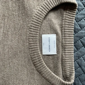 Beige merinoulltröja från A Day's March - Säljer en stilren beige stickad tröja från A Day's March i mjuk merinoull. Tröjan har rund halsringning, ribbade muddar och lång ärm. Perfekt för lager-på-lager under höst och vinter.