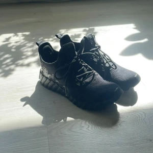 Svarta Adidas sneakers med grov sula - Säljer ett par svarta Adidas sneakers med chunky, räfflad sula och tydlig logga på sidan. Ovandelen är i mesh-liknande syntetmaterial och skorna har snörning. Perfekta för dig som gillar sportig och modern stil.