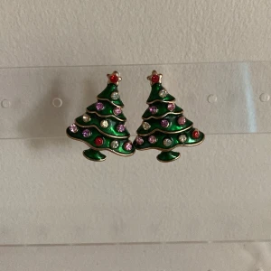 Julgransörhängen med strass - Superfina örhängen formade som julgranar i grön metall med färgglada strasstenar i rött, rosa och vitt. Perfekta för att maxa julkänslan med en lekfull och glittrig touch. Fästs med klassisk plupp.