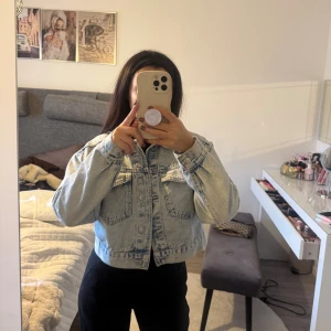 Croppad ljusblå jeansjacka - Säljer en croppad ljusblå jeansjacka med klassisk krage och stora bröstfickor. Jackan har knappar framtill och långa ärmar med en loose fit. Perfekt för dig som vill ha en chill och trendig vibe till din outfit.