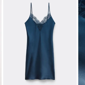 Intimissimi Blå satinklänning  - Supersnygg marinblå kort satinklänning med tunna axelband och v-ringning dekorerad med spets. Klänningen har en slimmad passform och glansigt material som ger en lyxig känsla. Perfekt för dig som vill sticka ut med en elegant och trendig look.