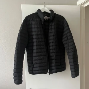 Svart pufferjacka från Colmar - Säljer en svart pufferjacka från Colmar. Jackan har horisontella quiltade sömmar, hög krage och dragkedja framtill. Lätt och smidig modell med två fickor med dragkedja. Perfekt för kyliga dagar. Skick 9/10 typ orörd. Storlek 52/L