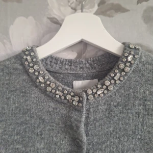 Grå kofta med diamanter från H&M - Kortärmad grå kofta från H&M i stickat material. Rund halsringning dekorerad med glittrande diamanter och knäppning framtill. ANNVÄND ENDAST 1 GÅNG! ☺️💕