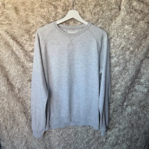 Ljusgrå sweatshirt från Pier One - En stilren ljusgrå sweatshirt från Pier One med rund halsringning och ribbade muddar vid ärmslut och nederkant. Tröjan är i mjuk bomullsblandning och har klassisk passform med långa ärmar. 