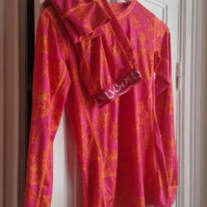 Underställ set S Kari Traa - Säljer en färgstark långärmad träningströja och byxor från Kari Traa i rosa och orange med blommigt mönster. Tröjan är i stretchigt material av polyester och elastan, perfekt för träning eller som första lager ute. 