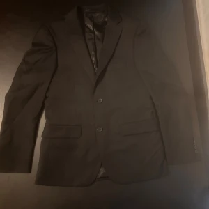 Svart kavaj slim fit från Dressmann XS - Säljer en svart kavaj från Dressmann i slim fit-modell. Klassisk design med två knappar framtill, fickor med lock och slät baksida. Fodrad insida för extra komfort. Ca strl XS