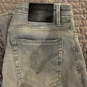 Grå jeans från Dondup, storlek 29 - Snygga grå jeans från Dondup i storlek 29. Jeansen har en ljus tvätt, klassisk femficksdesign och silverfärgade detaljer. Tillverkade i Italien och i mjukt jeanstyg som sitter skönt. Perfekta för dig som gillar stilrena och moderna jeans.