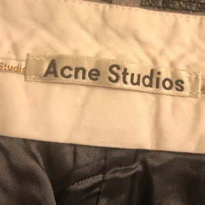 Grå kostymbyxor från Acne Studios - Snygga grå kostymbyxor från Acne Studios i ullmix med 5% kashmir. Byxorna har klassisk rak passform, hällor för bälte och pressveck. Perfekta för en clean och stilren look. Materialet är 75% ull, 20% nylon och 5% kashmir.