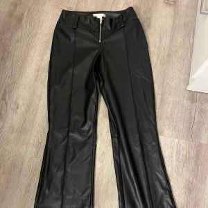 Svarta bootcut skinnbyxor - Snygga svarta byxor från Gina Tricot i skinnimitation med bootcut-ben och markerade sömmar framtill. Byxorna har medel/lowwaist midja, bälteshällor och en silverfärgad dragkedja framtill för en edgy look. Dom är super gosiga inuti vilket är perfekt nu till dom lite kyligare tiderna! OPS! Har sytt in midjan typ 2cm på varje sida men är nästan säker att de går att sprätta upp man skulle vilja de. Dessa byxor passar både till vardags men också festliga tillfällen! Inte fast pris!🩵🩷
