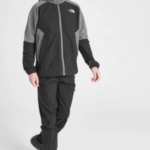 Svart och grå vindjacka från The North Face - Säljer en stilren vindjacka från The North Face i svart och grått. Jackan har huva, dragkedja framtill och logga på bröstet och ryggen. Perfekt för dig som gillar streetwear och vill ha en funktionell jacka med cool look.