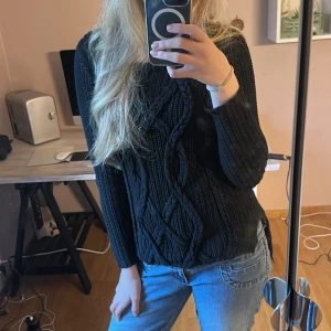 Svart kabelstickad tröja - Säljer en svart kabelstickad tröja med grov ribbstickning och snygga flätade detaljer framtill. Tröjan har lång ärm och en lite längre, rundad baksida. Perfekt för lager-på-lager och chill höst- eller vinterstil. Säljer för ärmarna är för korta på mig ❤️❤️❤️