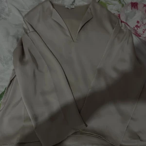 Beige sidenliknande skjorta Stockh LM - Snygg beige skjorta från Stockh LM Studio i storlek M. Skjortan har lång ärm, v-ringad krage och ett lyxigt, slätt material med sidenkänsla. Perfekt för dig som gillar stilrena och minimalistiska plagg.