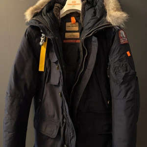 Parajumpers kodiak mörkblå dunjacka med päls - Äkta Parajumpers kodiak dunjacka i mörkblått med äkta päls på huvan, ikonisk gul rem och parajumper patch på ärmen. Jackan har flera fickor, dragkedja och knappar framtill samt quiltat foder. Perfekt för kalla dagar och riktigt snygg streetstil. Skriv privat för mer bilder eller andra funderingar. (Nypris 12 000kr)
