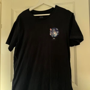 Svart Levi's t-shirt med blommigt tryck - Svart t-shirt från Levi's i storlek L med ett snyggt blommigt tryck i cirkelform på bröstet och texten 'Second Nature'. Klassisk rund hals och korta ärmar. Tillverkad i mjuk bomull som är skön mot huden. Perfekt för dig som gillar stilrena plagg med en twist.